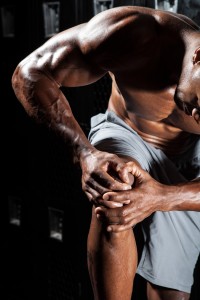 Portrait of a muscle fitness man reaching for his knee in pain