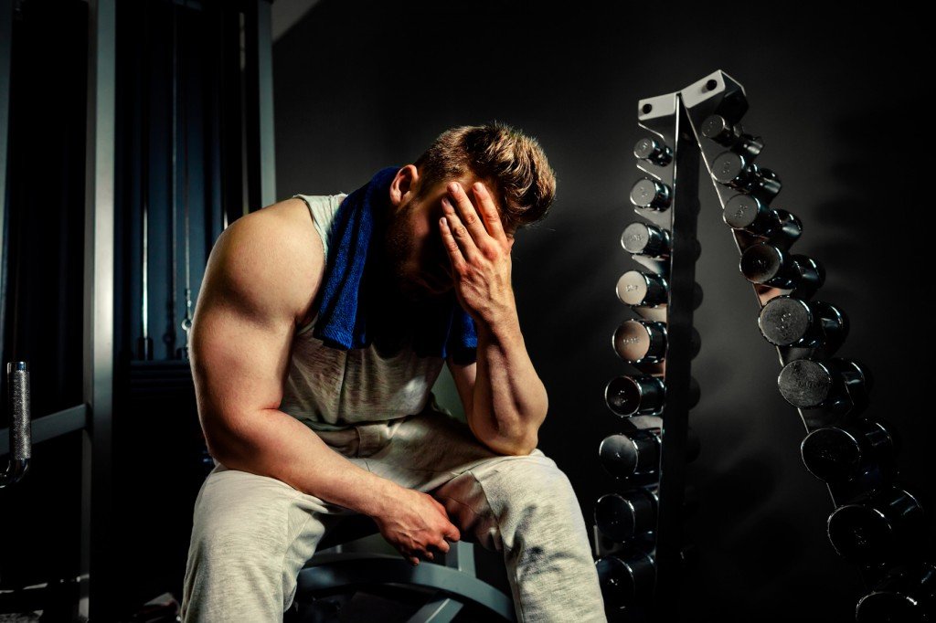 tired bodybuilder athlete with protein shaker and towel in gym