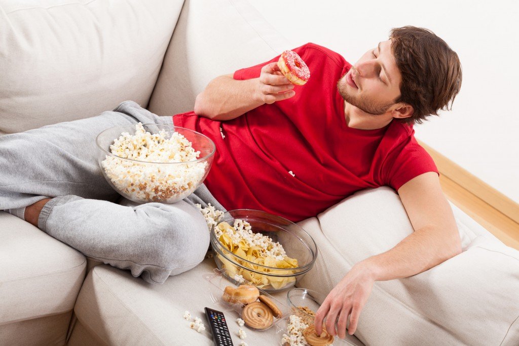 A man lying on a couch with sweets and popcorn in a mess