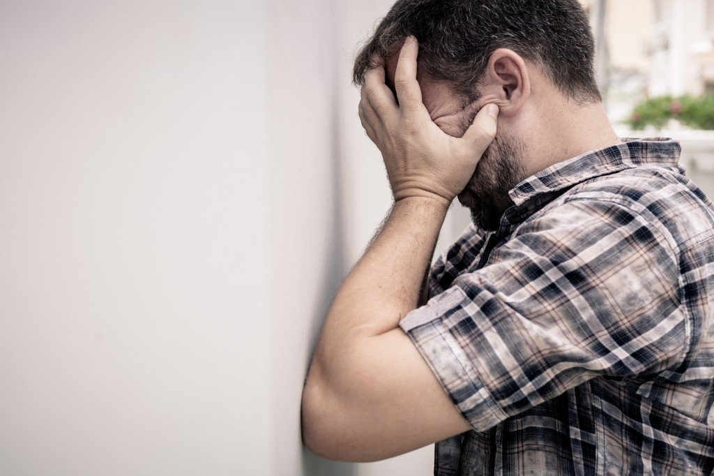 portrait one sad man standing near a wall and covers his face